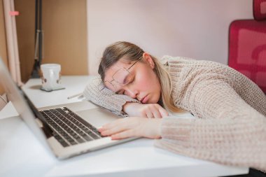 Yorgun bir kadın masada uyuyor, elleri dizüstü bilgisayar başında, kafa dinleniyor. Beyaz masada uyuyan bir kadınla rahat bir ev düzeni, eğik gözlükler ve yumuşak kırmızı sandalyede gevşek bir şekilde dinleniyor..