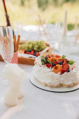 Beyaz krema tepeleri, turuncu kayısılar, kırmızı ahududular, yabanmersini ve açık hava pikniği için hazırlanmış nane yapraklı zarif pavlova tatlısına yakın plan.