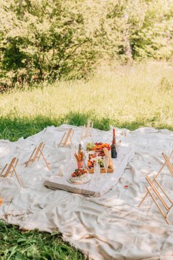 Açık hava piknik battaniyesi, boya sehpaları, palavra pastası ve taze mevsimlik meyveler. Tahta sehpalar, meyve tepsileri, köpüklü bardaklar, mumlar ve yaz aylarında sosyal boyama etkinliği için düzenlenen pasta manzarası geniş.