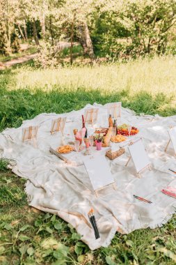 Özel sehpalar, fırçalar ve parlak doğal ortamdaki beyaz kumaş üzerinde renkli atıştırmalıklarla resim yapmak için rahat bir açık hava pikniği..