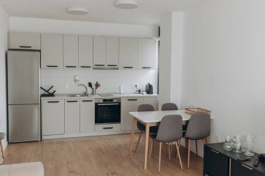 Entegre cihazlar, mat dolaplar ve nötr renk paleti ile kompakt mutfak içi. Dört vurgu alanı işlevsellik ve stil için yemek alanı. Ahşap zemin, yemek masası ve tarafsız tonlarda dahili dolapları olan modern aydınlık mutfak..