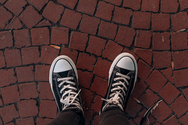 Два черных высоких кроссовки с белыми шнурками на красной мощеной мостовой поверхности, показывающие городской образ жизни обувь и текстурированный каменный фон обычно встречаются в европейских пешеходных районах.