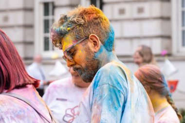 Belfast, Kuzey İrlanda - 17 Ağustos 2024: Geleneksel Mela Karnaval Geçidi, sakallı ve gözlüklü genç adam Holi tarzı boya tozu ile kaplandı.
