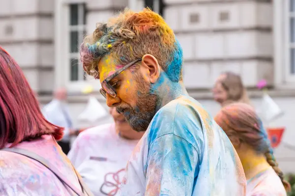 Belfast, Kuzey İrlanda - 17 Ağustos 2024: Geleneksel Mela Karnaval Geçidi, sakallı ve gözlüklü genç adam Holi tarzı boya tozu ile kaplandı.