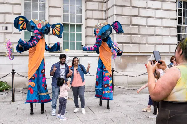 Belfast, Kuzey İrlanda - 17 Ağustos 2024: Belfast Mela çok kültürlülük kutlamalarının sonunda aile, belediye binasında bir çift mavi fille fotoğraf çektirmek için poz veriyor..