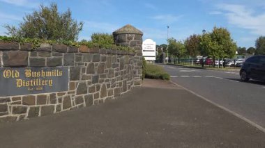 Bushmills, Kuzey İrlanda - 18 Ağustos 2025: Mavi gökyüzü ile güneşli bir günde Old Bushmills İrlanda Viski Fabrikası 'nın girişinden ayrılan araba ziyaretçileri