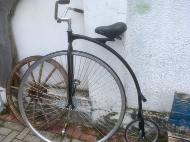 Önünde büyük bir tekerlek, arkasında da duvara yaslanmış küçük bir bisiklet forumu.