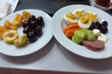 İki beyaz tabakta dilimlenmiş sebze, yumurta ve sosis, kiraz ve kayısı var. Afiyet olsun..