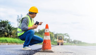 İnşaat işçisi trafik konisi yakınındaki cep telefonundan kontrol ediyor.