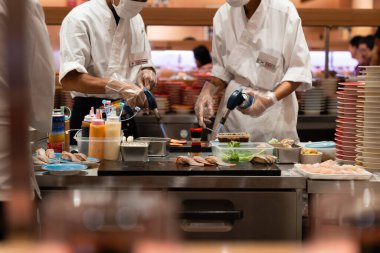 Usta şefler taze malzemeler, kaynak makineleri ve soslar kullanarak özenle suşi yapıyorlar. Canlı restoran atmosferi Japon mutfak sanatının cazibesini artırıyor.