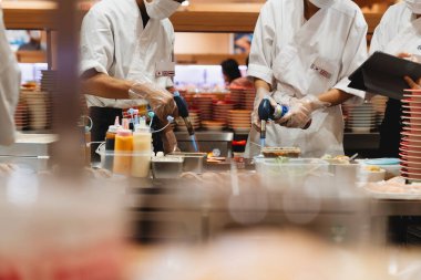 Usta şefler taze malzemeler, kaynak makineleri ve soslar kullanarak özenle suşi yapıyorlar. Canlı restoran atmosferi Japon mutfak sanatının cazibesini artırıyor.