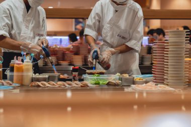 Usta şefler taze malzemeler, kaynak makineleri ve soslar kullanarak özenle suşi yapıyorlar. Canlı restoran atmosferi Japon mutfak sanatının cazibesini artırıyor.