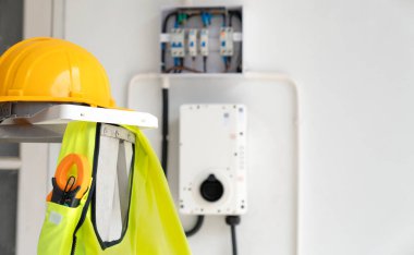 Elektrikli aletler, sarı kask, güvenlik yeleği ve klemp sayacı dahil, elektrik panelinin yanında. Güvenli ve verimli ev EV duvar şarj cihazı kurulumu için mükemmel.