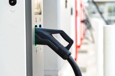 Yüksek hızlı şarj istasyonuna yerleştirilmiş bir elektrikli aracın (EV) yakın çekimi. Aydınlatılmış şarj portu aktif güç transferini gösteriyor. Bu resim modern EV altyapısını, temiz enerji çözümlerini ve gelecekteki