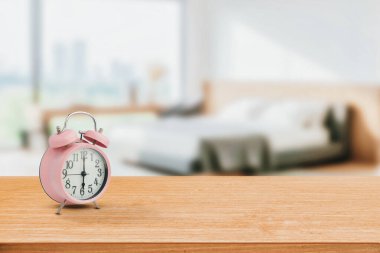 Ahşap bir masaya yerleştirilmiş, modern yatak odası arka planı bulanık, pembe çalar saat. Zaman, sabah rutini ya da yaşam tarzı içeriğindeki iç dekorasyon temaları için mükemmel.