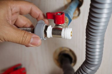Kırmızı kapakçığa esnek bir su borusunu, dolgu bandıyla bağlayan elin yakın çekimi. Cihaz montajı, tesisat, DIY ve ev bakımı için ideal. Güvenli bağlantılara odaklan.