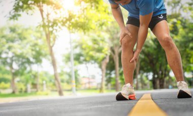 Sporcu öne eğiliyor, baldır kaslarını sıkıyor güneşli açık yolda koşarken kendini rahatsız hissediyor.