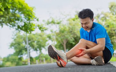 Acıyla yüzünü buruşturan adam, doğanın arka planında koşarken kazadan sonra bacak kaslarını kavrıyor.