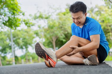 Acıyla yüzünü buruşturan adam, doğanın arka planında koşarken kazadan sonra bacak kaslarını kavrıyor.
