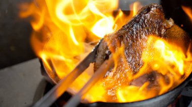 Pikanha bifteğinin sıcak dökme demir tavada kızarması ve çıtır çıtır kıtır kabuk dokusu için yoğun alevler.