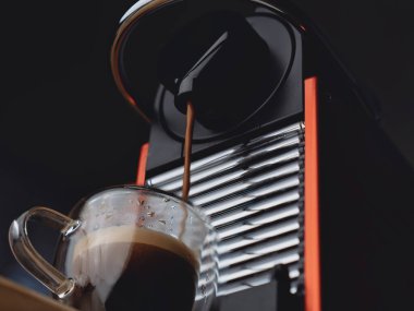 Modern kırmızı espresso makinesi yüksek kontrastlı aydınlatma ile cam bardağa kahve dağıtıyor.