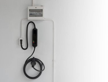 Ev duvarı sarmalanmış kablo ve bağlı kontrol kutusuyla acil durum elektrikli araç şarjı takılı.