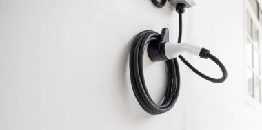 Modern bir garajda ya da şarj istasyonunda duvara düzgünce sarılmış siyah elektrikli aracı kapat.