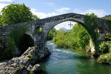 Yeşilliklerle kaplı antik taş köprü, yemyeşil ağaçlar ve manzarayla çevrili sakin bir nehir boyunca uzanır. Güzel tarihi mimari.