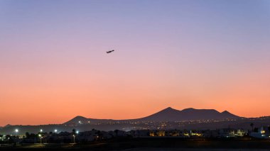 Bir ATR uçağı Lanzarote 'un üzerindeki alacakaranlık gökyüzüne yükseliyor. Şehir ışıkları altta parlıyor ve dağlar gün batımının değişen renklerine karşı gölgeleniyor..