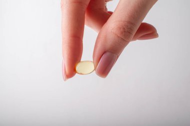 Beyaz arka planda vitaminler tutan dişi kapsül. Omega 3 'ü tutan parmaklar, yakın plan. Sağlık sigortası, beslenme takviyeleri, D vitamini, hastalıkların tedavisi. Yüksek kalite fotoğraf