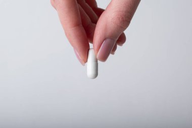 Kadın kapsülü beyaz arka planda tutuyor. Parmaklar hapları tutuyor, yakın plan. Sağlık, beslenme takviyeleri, vitaminler, depresyon ve hastalıkların tedavisi kavramı. Yüksek kalite fotoğraf