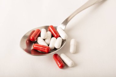 Kaşıkta ilaç. Kırmızı ve beyaz kapsüller arka planda izole edilmiş. Vitaminler, takviyeler, antibiyotikler, alerji hapları. Tıp, sağlık hizmeti konsepti. Grip hastalıkları. Yüksek kalite fotoğraf