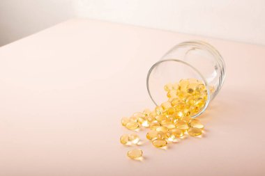 Yumuşak kapsüller pembe arka plandaki bardaktan dökülür. Omega 3 balık yağı, vitaminler. Morina yağı kapanışı. Sağlık sigortası, takviye malzemeler, D vitamini. Kopya alanı, afiş. Yüksek kalite fotoğraf