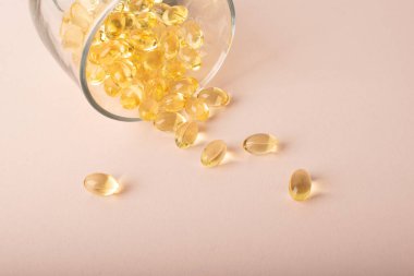 Omega 3 balık yağı pembe arka plandaki bardaktan akıyor. Yumuşak kapsüllerde vitaminler, morina yağı. Sağlık sigortası, takviye malzemeler, D vitamini. Kopya alanı, afiş. Yüksek kalite fotoğraf