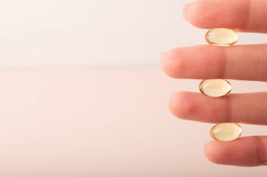 Pembe arka planda el ele tutuşan vitaminler yumuşak kapsül. Omega 3 'ü tutan kadın parmaklar, yakın plan. Sağlık sigortası, beslenme takviyeleri, D vitamini, hastalıkların tedavisi. Yüksek kalite fotoğraf