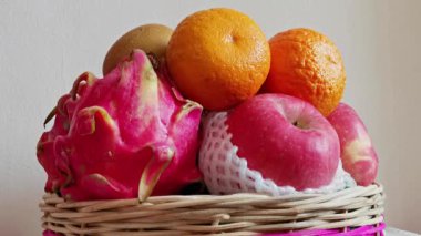 Taze elma, portakal, ejderha meyvesi ve kivi dolu bir meyve sepetinin olduğu canlı bir hayat. Renkli meyveler hasır bir sepete konur ve görsel olarak çekici bir görüntü oluşturur.