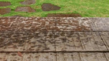 Yıpranmış ahşap kalasların doğal dokusunu keşfedin. Yeşil çimen ve yağmur damlalarıyla çelişen tahtalar. Basitliği ve doğayla bağlantıyı vurgulayan arka plan ve görsel unsurlar için mükemmel..