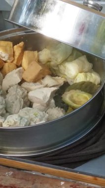 This video shows the preparation of Indonesian street food siomay, a popular steamed dumpling dish with peanut sauce. The vendor prepares and serves the food with fresh ingredients.