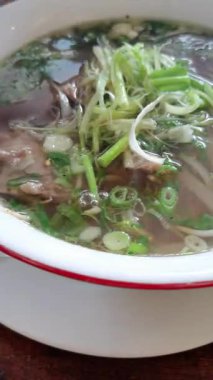Experience authentic Vietnamese Pho, a rich, flavorful noodle soup. Witness the careful arrangement of fresh herbs and vegetables, enriching the savory broth and creating an aromatic flavor.