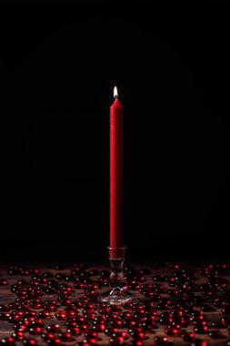 Cam bir şamdanın üzerinde yanan kırmızı mum. Masadaki kırmızı mücevherlerle çevrili..
