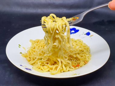 Beyaz tabakta kaynamış hazır şehriye, siyah arka planda izole edilmiş. Elin çatallı erişteyi alır. Fast food. Modern yemekler. Düz üst görünüm