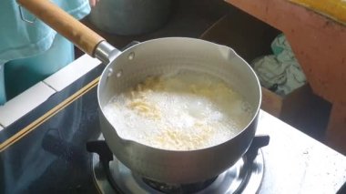 POV elleri evde hazır şehriye çorbası pişiriyor. Asyalı kadın eli evdeki kaynar suya kuru erişte koyup karıştırıyor. Gaz sobasında buharlı yemek..