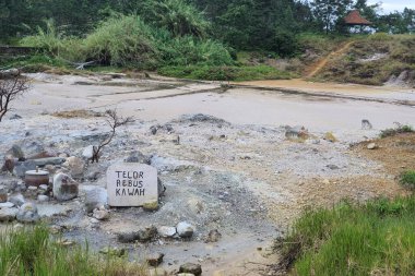 A sign translated as Deviled egg volcano, people who sell boiled egg from the geothermal hot spring of Kawah Sikidang, Dieng, Central Java clipart