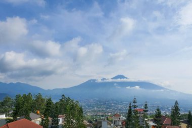 Majestic Mountain Views: Huzurlu Rolling Hills ve Houses manzarası, Uzak Tepeler ve Yumuşak Bulutlu Mavi Gökyüzü. Resimli Sahne, Nefes Kesen Panorama, Huzurlu Atmosfer.