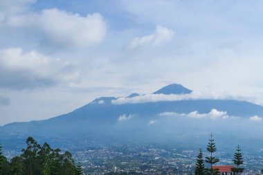 Görkemli Dağlar Bulutlarla çevrili: Rolling Hills ve City Skyline 'ın Mavi Gök Altında Huzurlu Manzarası