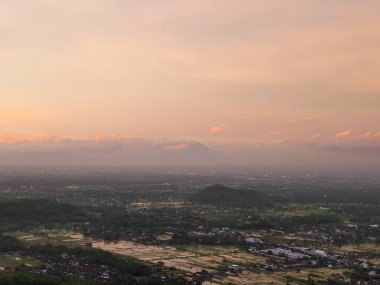 Sunset Aerial View: Serene Peyzaj of Rice Paddies, Distant Mountains, and Cityscape at Dusk. Huzurlu Altın Saat Panoraması, Kırsal ve Kentsel Manzaranın Güzelliği.