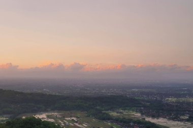 Stunning Aerial View Reveals Serene Sunset Over Expansive Cityscape and Lush Green Fields, Displaying Breathtaking Panorama of Nature and Urban Development with Tranquil Colors at Golden Hour.  clipart