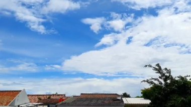 Evlerin çatısında hareket eden bulutların zamanı dinamik bir gökyüzü sahnesi yaratıyor.