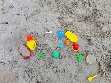 Kum Sahili 'nde Terk Edilmiş Renkli Plastik Oyuncaklar: Tekneler, Bloklar ve Güneş' te Eğlendikten Sonra Geride Bırakılan Kovalar, Kum ve Suya Açılan Aşınma İzleri Gösteriliyor.