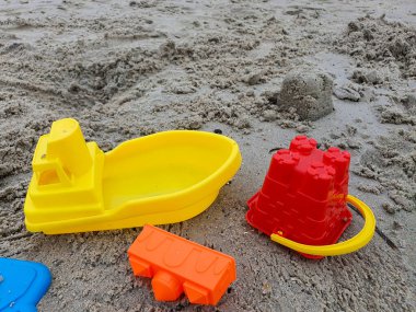 Kumsalda Dinlenen Renkli Plastik Oyuncaklar: Sarı Tekne, Kırmızı Şato, Turuncu Bloklar, Mavi Kürek, Yaz Eğlencesi ve Yaratıcı Oyun Zamanı